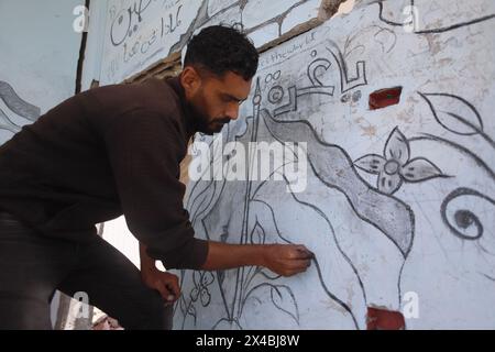 Artista palestinese Ghassan Habboub, chi si è rifugiato nella città di Rafah a causa degli attacchi israeliani, disegna immagini della bandiera palestinese e della moschea di al-Aqsa che simboleggiano la solidarietà a Gaza con il carbone sul muro di un edificio che è stato pesantemente danneggiato a seguito degli attacchi a Rafah, Gaza, il 30 aprile 2024. Martedì scorso le Nazioni Unite hanno avvertito che un assalto israeliano a Rafah nella Striscia di Gaza era "all'orizzonte immediato” e che i progressi "incrementali” compiuti da Israele in materia di accesso agli aiuti all'enclave non potevano essere utilizzati per preparare o giustificare un'operazione. Il Segretario generale delle Nazioni Unite Antonio Guterres ha presentato ricorso Foto Stock