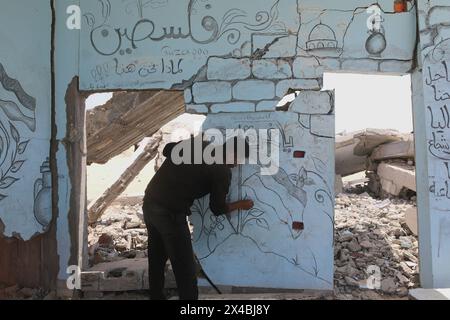Artista palestinese Ghassan Habboub, chi si è rifugiato nella città di Rafah a causa degli attacchi israeliani, disegna immagini della bandiera palestinese e della moschea di al-Aqsa che simboleggiano la solidarietà a Gaza con il carbone sul muro di un edificio che è stato pesantemente danneggiato a seguito degli attacchi a Rafah, Gaza, il 30 aprile 2024. Martedì scorso le Nazioni Unite hanno avvertito che un assalto israeliano a Rafah nella Striscia di Gaza era "all'orizzonte immediato” e che i progressi "incrementali” compiuti da Israele in materia di accesso agli aiuti all'enclave non potevano essere utilizzati per preparare o giustificare un'operazione. Il Segretario generale delle Nazioni Unite Antonio Guterres ha presentato ricorso Foto Stock
