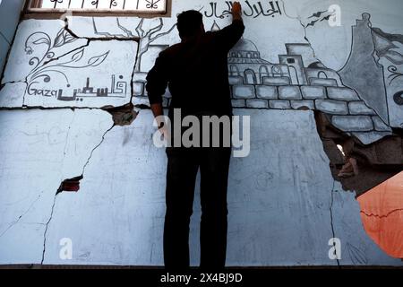Artista palestinese Ghassan Habboub, chi si è rifugiato nella città di Rafah a causa degli attacchi israeliani, disegna immagini della bandiera palestinese e della moschea di al-Aqsa che simboleggiano la solidarietà a Gaza con il carbone sul muro di un edificio che è stato pesantemente danneggiato a seguito degli attacchi a Rafah, Gaza, il 30 aprile 2024. Martedì scorso le Nazioni Unite hanno avvertito che un assalto israeliano a Rafah nella Striscia di Gaza era "all'orizzonte immediato” e che i progressi "incrementali” compiuti da Israele in materia di accesso agli aiuti all'enclave non potevano essere utilizzati per preparare o giustificare un'operazione. Il Segretario generale delle Nazioni Unite Antonio Guterres ha presentato ricorso Foto Stock