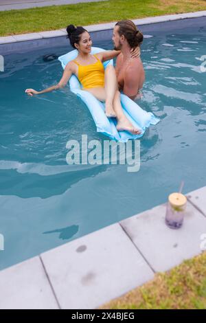 Coppie diverse che si rilassano all'aperto in piscina, donne su un galleggiante, spazio fotocopie. Goditi il sole, indossando occhiali da sole e sorridendo, circondato da un blu sereno Foto Stock