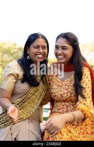 Madre asiatica e figlia adolescente stanno ridendo insieme all'aperto. Entrambi hanno i capelli scuri e la giovane donna indossa un abito a motivi rossi, inalterato Foto Stock