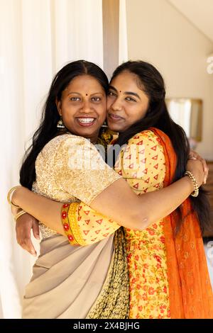 Madre indiana e figlia adolescente, abbracciati a casa, entrambi sorridenti. Madre in sari, figlia adolescente in un salwar kameez, che si gode un momento caldo togeth Foto Stock