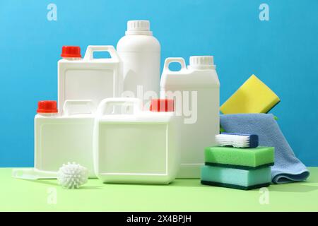 Set di diversi contenitori di detergente visualizzati con spazzole, spugne e panni su sfondo blu. Scena pubblicitaria per la pulizia di prodotti con mockup Foto Stock