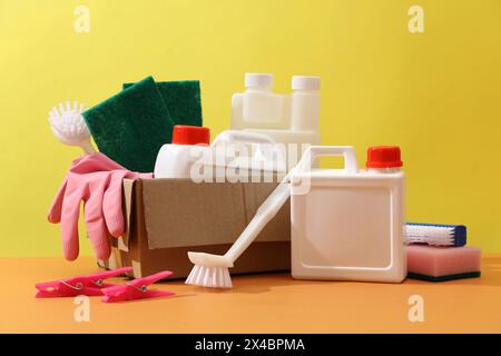 Vista frontale del set di diversi detergenti visualizzata su sfondo giallo. Contenitori in plastica bianca senza etichetta decorati con spazzole, spugne e. Foto Stock