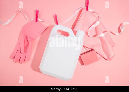Idea creativa per la pulizia di prodotti pubblicitari. Un contenitore di detergente bianco in plastica con guanto in gomma e spugnette abrasive appese su un nastro utilizzando un coagulo Foto Stock