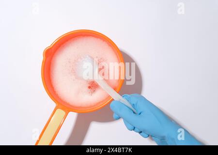 Indossare guanti di gomma con una spazzola per WC immersi in un secchio di plastica riempito con soluzione di sapone su sfondo bianco. Concetto di pulizia. Inizio vi Foto Stock