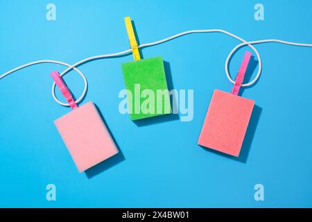 Vista dall'alto di una corda con tre clothespins che tengono in posizione tre spugne di tre diversi colori su sfondo blu. Copia spazio per la pubblicità Foto Stock