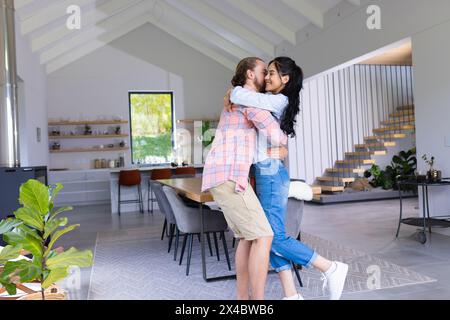 Diverse coppie che abbracciano una casa moderna. Donna birazziale con lunghi capelli scuri e uomo caucasico con barba che condivide un momento di amore, inalterato Foto Stock