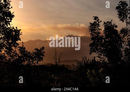 Vista distante dall'est dell'Etna in Sicilia, Italia. In una calda serata di fine agosto, i raggi del sole che tramonta retroilluminano i pennacchi di fumo e le nuvole di gas solforoso che fuoriescono dai crateri sommitali dell'Etna. Foto Stock