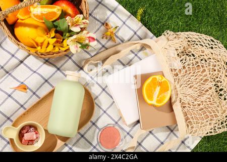 Cestino da picnic con frutta e fiori decorato con sacchetti in rete libri, scatola blush e marmellate su tessuto a scacchi. Un flacone vuoto visualizzato sul WO Foto Stock