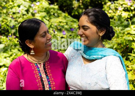 Madre indiana e figlia adolescente sorridenti l'un l'altro all'aperto. Entrambi con i capelli scuri, giovane donna con il top blu, donna matura in rosa, inalterata Foto Stock