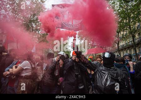 1 maggio 2024, Parigi, Francia. Un manifestante vestito di nero il giorno di maggio regge un'esplosione di fumo rosso davanti a una bandiera dell'Action Antifasciste. Crediti: Jay Kogler/Alamy Live News Foto Stock