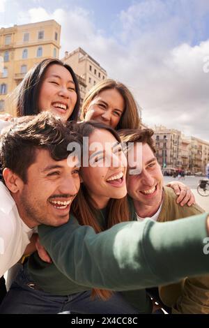 Gruppo di giovani felici che fanno selfie sorridenti insieme giorno di sole in città all'aperto. Foto Stock