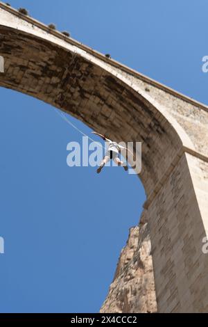 Vista dall'angolo basso di una persona che salta da uno storico ponte di pietra. Concetto di sport d'avventura. Nessuna paura Foto Stock