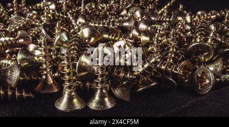 Un mucchio di viti metalliche gialle su sfondo nero. Sfondo delle viti metalliche. Foto Stock