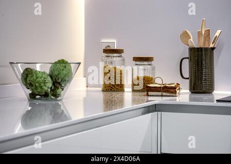 Angolo di una cucina con armadi bianchi, ripiani in finta pietra e una ciotola di vetro con carciofi freschi Foto Stock