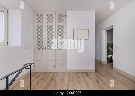 Scala con gradini in legno di quercia di una casa indipendente con ringhiera in metallo di stile minimalista nero, pareti bianche e un armadio a muro con porte a reticolo Foto Stock