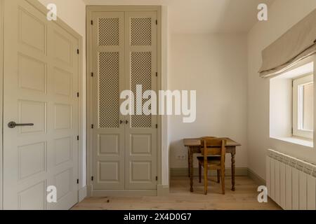 Una camera con un armadio a muro con porte a reticolo in legno e una scrivania in legno vintage con sedia coordinata Foto Stock