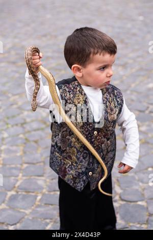 Un giovane ragazzo partecipa al rito dei serpenti e alla festa di San Domenico. La più famosa e misteriosa celebrazione folcloristica abruzzese è un evento in cui i costumi pagani e la tradizione cristiana si fondono: La devozione a San Domenico, protettore contro il morso dei rettili, si intreccia con il rituale arcaico dei "serpari". Questa usanza è legata ai riti pagani dei Marsi, un antico popolo italico. In epoca contemporanea, si celebra in onore di San Domenico, che si ritiene sia il protettore contro mal di denti, morsi di rettili e rabbia. La cerimonia, ora fissata il primo di maggio ciascuna Foto Stock