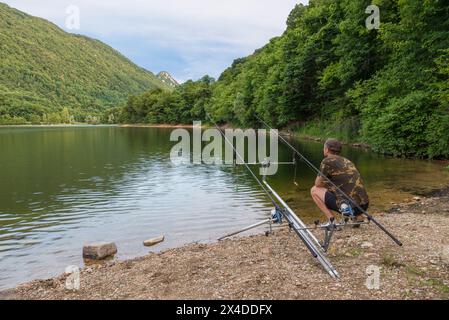 Avventure di pesca, pesca delle carpe. Il pescatore d'estate pesca in un piccolo lago tra le montagne e le verdi foreste Foto Stock