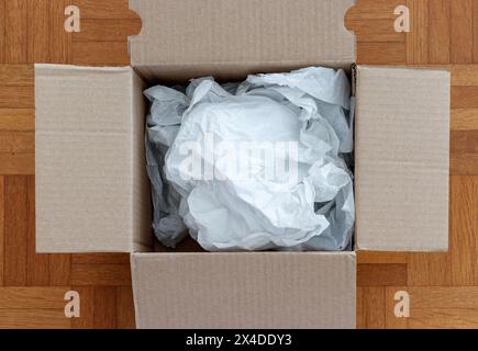 Scatola di cartone riempita con carta da imballaggio per spedizioni su un pavimento in legno, vista direttamente dall'alto in stile piatto. Trasporto merci e commercio elettronico Foto Stock