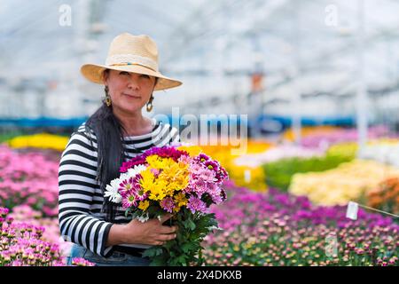 Una donna colombiana porta un mazzo di fiori disposti di crisantemi in una fattoria di fiori recisi a Rionegro, Colombia, il 15 marzo 2024. Foto Stock