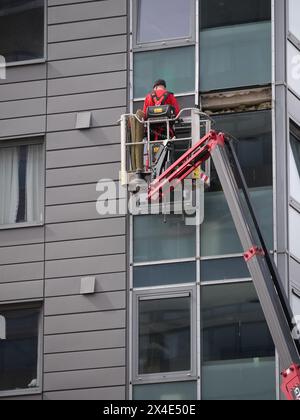 Lavoratore in una piattaforma rialzata che esegue interventi di manutenzione reattivi per la riparazione del rivestimento esterno di un edificio alto. Plymouth, Regno Unito Foto Stock