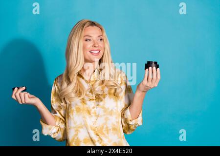 Foto di attraente donna matura tenere aperto l'aspetto crema spazio vuoto vestiti eleganti abiti formalwear isolati su sfondo di colore ciano Foto Stock