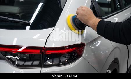 Processo di lucidatura della superficie bianca della carrozzeria della vettura con una lucidatrice orbitale. Foto Stock