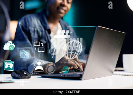 Donna afroamericana che lavora da casa con un laptop, concetto di connettività online. Dipendente remoto che utilizza la tecnologia di realtà aumentata per visualizzare le funzioni software dei notebook Foto Stock