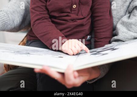 Un bambino che indica un libro mentre un genitore lo legge. Il bambino indossa una camicia rossa Foto Stock