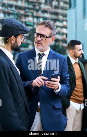 Gli uomini d'affari caucasici del gruppo si sono riuniti parlando seriamente utilizzando il telefono cellulare durante le pause di lavoro all'aperto. Foto Stock