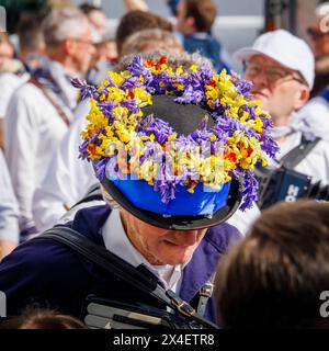 Un fisarmonicista del Blue Ribbon indossa un cappello con campanelli e cowslips per il festival "Obby 'Oss", un evento popolare annuale che si tiene il giorno di maggio a Padstow, Cornovaglia Foto Stock