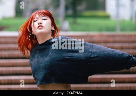 Donna coreana con i capelli rossi perduti in un movimento di danza fluente su una scala della città Foto Stock