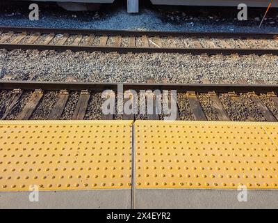 Le mattonelle di avvertimento gialle urtano di fronte ai binari del treno Foto Stock