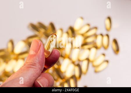 mano della donna che tiene in mano una pillola di olio di pesce con omega 3 di colore giallo dorato, un nutriente essenziale Foto Stock