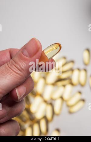 mano della donna che tiene in mano una pillola di olio di pesce con omega 3 di colore giallo dorato, un nutriente essenziale Foto Stock