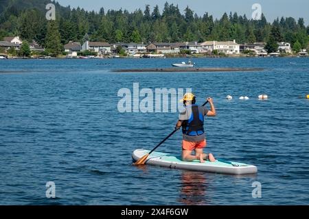Issaquah, Stato di Washington, Stati Uniti. Donna inginocchiata sul suo paddleboard, pagaiando lungo il lago Sammamish. (Solo per uso editoriale) Foto Stock