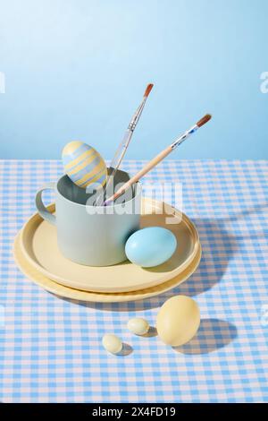 Uova di Pasqua dipinte a mano con piatti in ceramica, tazza e pennello decorati su sfondo azzurro. Idee per la decorazione delle uova per Pasqua, foto pubblicitarie Foto Stock