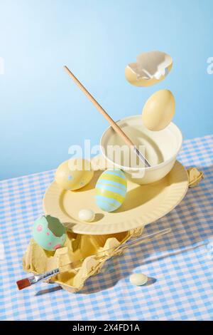 Idee creative per decorare le feste di Pasqua. Uova di Pasqua dipinte a mano, pennelli, piatto in ceramica e ciotola decorati su sfondo azzurro Foto Stock