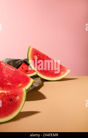 Vista frontale delle succose fette di anguria decorate su sfondo rosa con pietra grigia. L'anguria è come l'ultimo go-to estivo per quando sei rea Foto Stock