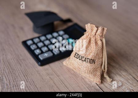 Immagine ravvicinata del cappello di graduazione, della calcolatrice e del sacchetto di denaro con L'ISTRUZIONE di parola. Concetto finanziario. Foto Stock