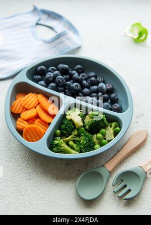 Ciotola in plastica per bambini con broccoli, mirtilli e carote. Alimenti sani per bambini nel recipiente Foto Stock