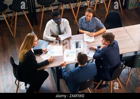 Il CEO donna dirige un team diversificato in una sessione di strategia in un ufficio moderno, con grafici e laptop per il processo decisionale basato sui dati. I professionisti si impegnano Foto Stock