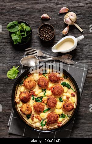 polpette di pollo toscano con gnocchi in salsa cremosa con pomodori secchi e foglie di spinaci in piatto da forno su tavola di legno scuro con ingredienti, Foto Stock