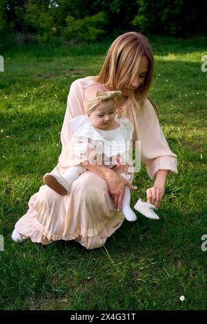 la madre mette le scarpe sulla sua bambina nel parco Foto Stock