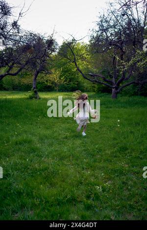 una bambina dai capelli lunghi corre nel giardino con un cestino pieno di fiori Foto Stock