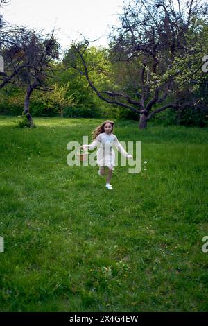 una bambina dai capelli lunghi corre nel giardino con un cestino pieno di fiori Foto Stock