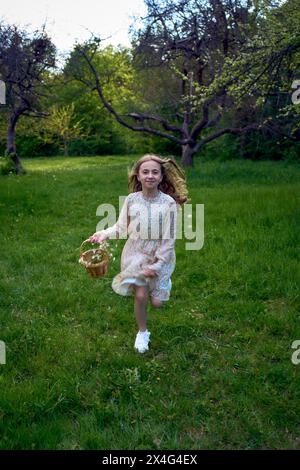 una bambina dai capelli lunghi corre nel giardino con un cestino pieno di fiori Foto Stock