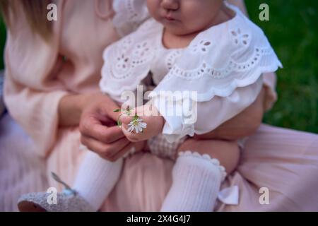 una bambina tiene un fiore tra le mani tra le braccia di sua madre Foto Stock